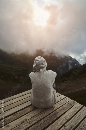Obraz na płótnie a girl in a grey hoodie sitting on a viewpoint and watching sunset in the mountains w salonie