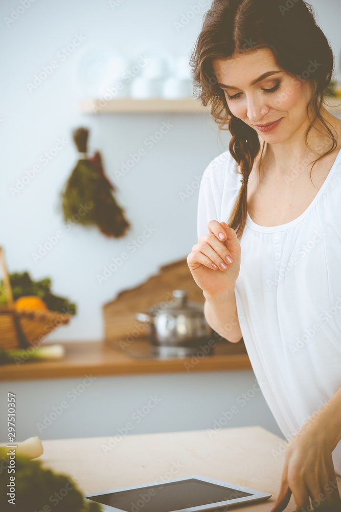 Young woman looking for a new recipe for cooking in a kitchen. Housewife is making online shopping by tablet computer and credit card Young woman looking for a new recipe for cooking in a kitchen. Housewife is making online shopping by tablet computer and credit card
