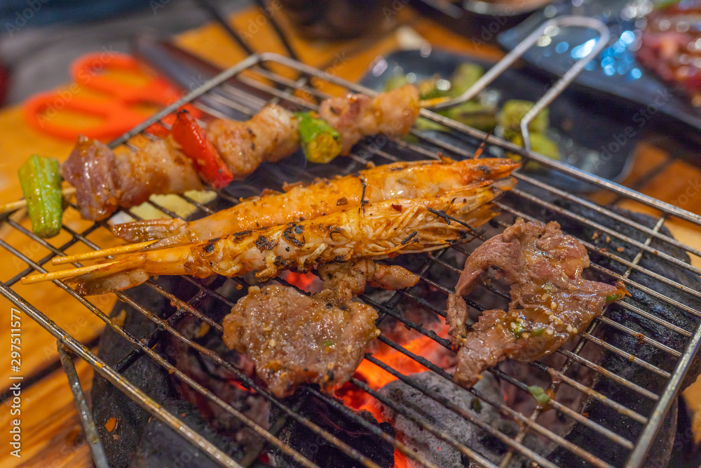 Meat slices, pork kebab and shrimp on flaming charcoal stove
