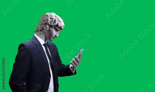 Modern art collage. Concept portrait of a  businessman  holding mobile smartphone using app texting sms message. Gypsum head of of Antinous. Man in suit. On a green background. photo