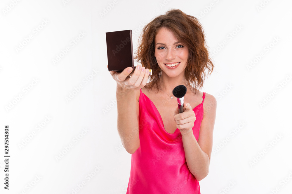 Young beautiful girl with wavy brown hair, clean skin, flat teeth, beautiful smile, in pink jersey, with makeup brush, powder and mirror makes makeup Young beautiful girl with wavy brown hair, clean skin, flat teeth, beautiful smile, in pink jersey, with makeup brush, powder and mirror makes makeup