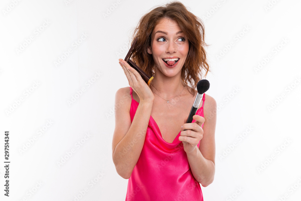 Young beautiful girl with wavy brown hair, clean skin, flat teeth, beautiful smile, in pink jersey, with makeup brush, powder and mirror makes makeup Young beautiful girl with wavy brown hair, clean skin, flat teeth, beautiful smile, in pink jersey, with makeup brush, powder and mirror makes makeup