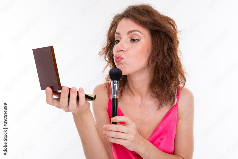 Young beautiful girl with wavy brown hair, clean skin, flat teeth, beautiful smile, in pink jersey, with makeup brush, powder and mirror makes makeup Young beautiful girl with wavy brown hair, clean skin, flat teeth, beautiful smile, in pink jersey, with makeup brush, powder and mirror makes makeup