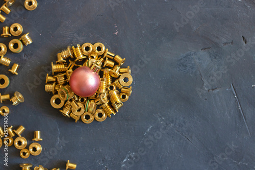 Round form made of gold pop rivet nuts ond lochnuts with pink christmas ball on it on black tectured chalk board. Horizontal copy space. Fasteners, screws and details. Top view. New year concept.