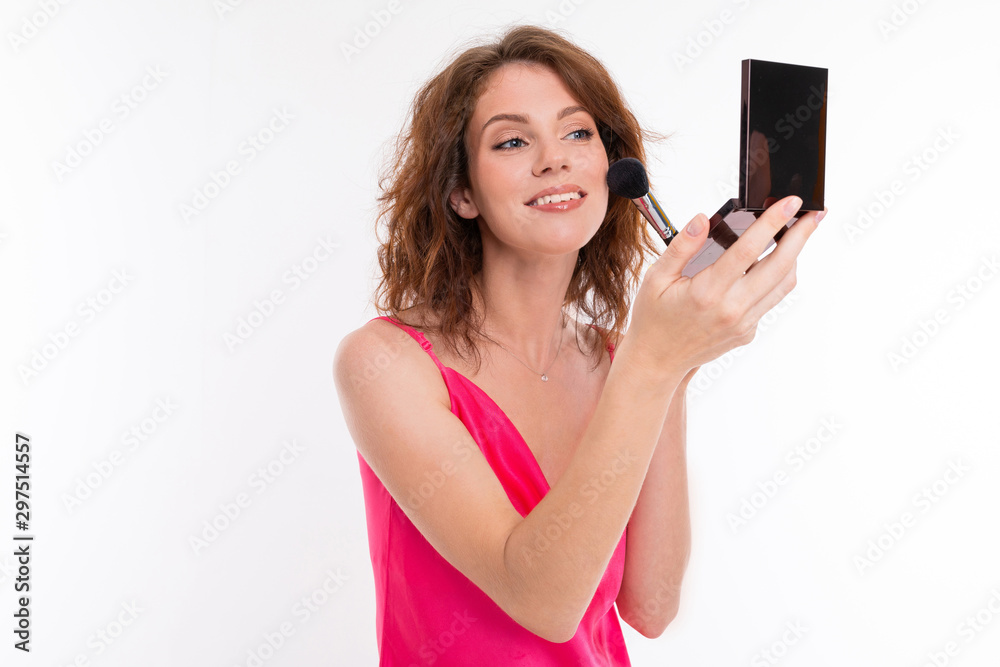 Young beautiful girl with wavy brown hair, clean skin, flat teeth, beautiful smile, in pink jersey, with makeup brush, powder and mirror makes makeup Young beautiful girl with wavy brown hair, clean skin, flat teeth, beautiful smile, in pink jersey, with makeup brush, powder and mirror makes makeup