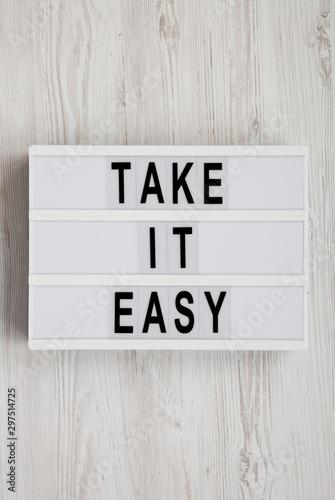 Fototapeta Naklejka Na Ścianę i Meble -  'Take it easy' words on a lightbox on a white wooden background, top view. Overhead, from above, flat lay. Close-up.