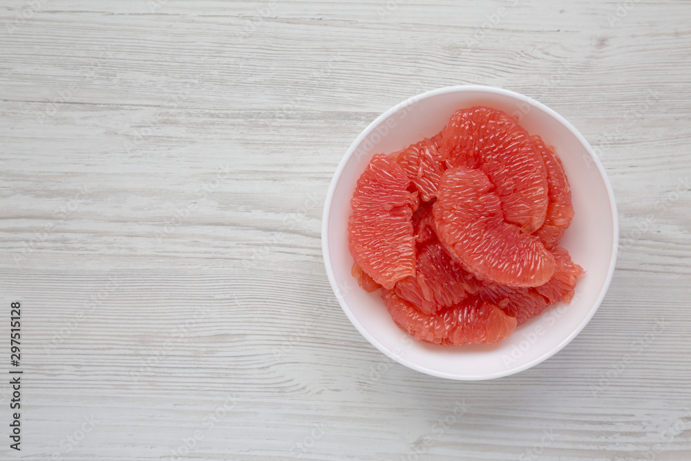 Red grapefruit slices in a white bowl on a white wooden background, overhead view. Flat lay, top view, from above. Copy space. Red grapefruit slices in a white bowl on a white wooden background, overhead view. Flat lay, top view, from above. Copy space.