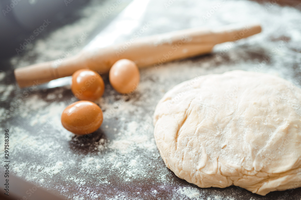 Dough, rolling pin, egg and flour on wooden table. Raw pizza dough with ingredients on the kitchen table. Dark background. Сooking concept. Dough, rolling pin, egg and flour on wooden table. Raw pizza dough with ingredients on the kitchen table. Dark background. Сooking concept.