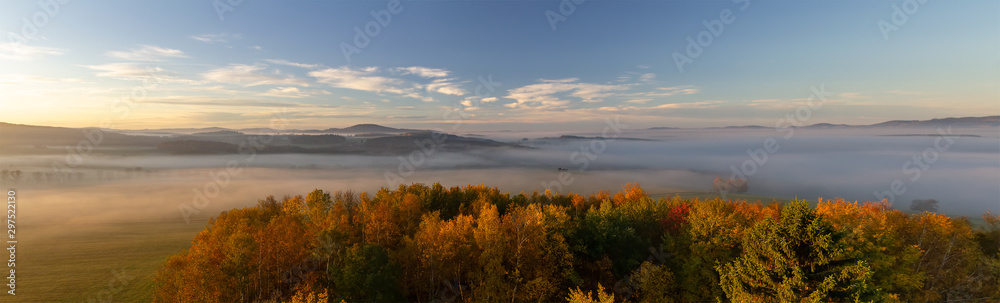 Aerial panoramic view to autumn foliage trees and meadow with misty fog and hill at sunrise, Czech landscape Aerial panoramic view to autumn foliage trees and meadow with misty fog and hill at sunrise, Czech landscape