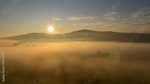 Aerial view to misty fog with path and hill at sunrise, Czech landscape