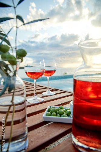 two glasses of rose wine with olives against blue water on a pier..