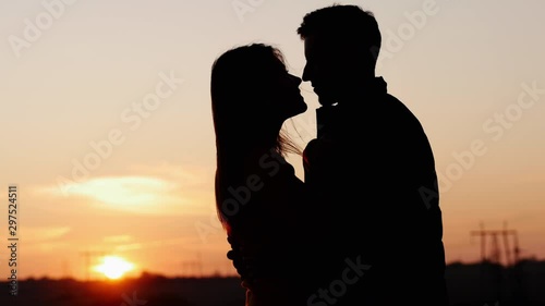 Silhouette of first tenderly kissing of adorable young couple in the field at sunset