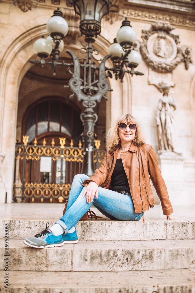 Woman tourist in jeans and a leather jacket is resting and enjoying the view on the steps of an old building