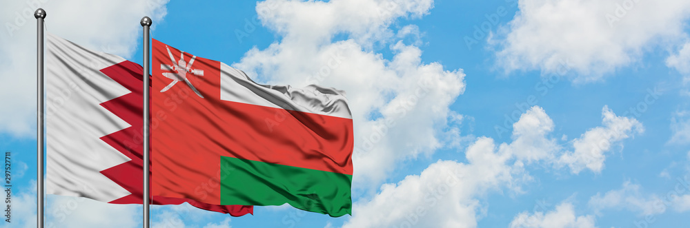 Naklejka premium Bahrain and Oman flag waving in the wind against white cloudy blue sky together. Diplomacy concept, international relations.