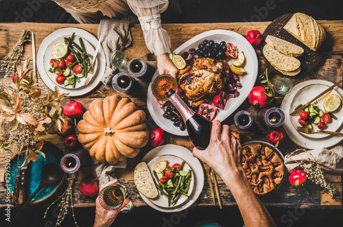 Thanksgiving party table setting. Flat-lay of people pouring champagne and celebrating at table with roasted chicken, vegetables, fig pie, fruit, candles over wooden table background, top view