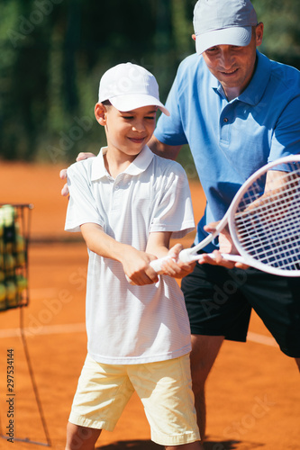 Tennis Lesson. Smiling Coach Explaining Tennis Technique to a Boy © Microgen