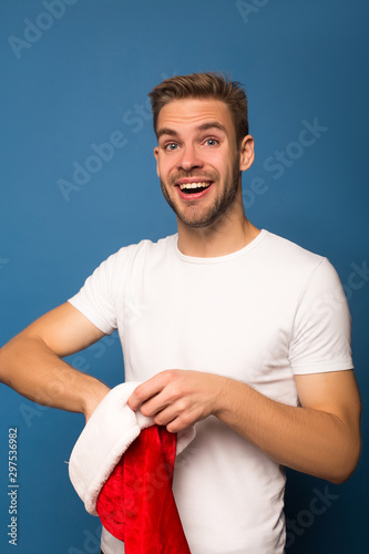 excited young man putting hand in santa hat isolated on blue