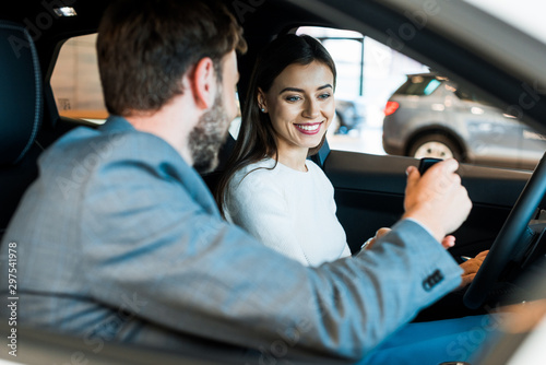 selective focus of cheerful woman looking at car key in hand of bearded man