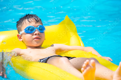 Asia boy wearing swimming goggles on yellow protrude in a swimming pool.