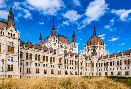 Daytime close up view of historical building of Hungarian Parliament in Budapest, Hungary, Europe with hungarian national flag on background of bright blue cloudy sky