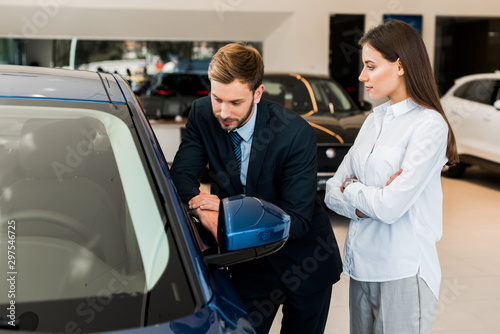 attractive woman standing with crossed arms near handsome bearded man in car showroom