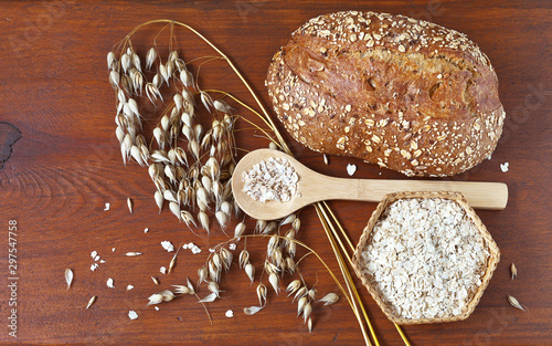 Wholesome oat food products: cereal bread and oatmeal in wicker bowl with ears of oat on wooden background. Healthy eat with dietary fiber. Rustic still life. Flat lay, top view, close-up, copy space photo