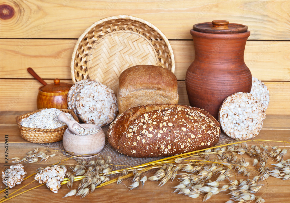 Rustic still life with traditional oat products: cereal bread, oat milk in clay jug, oatmeal and bread crisps on a wooden background. Healthy organic foods Rustic still life with traditional oat products: cereal bread, oat milk in clay jug, oatmeal and bread crisps on a wooden background. Healthy organic foods