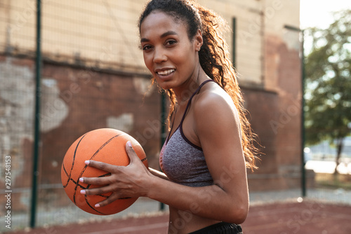 Image of joyful african american woman playing basketball at playground