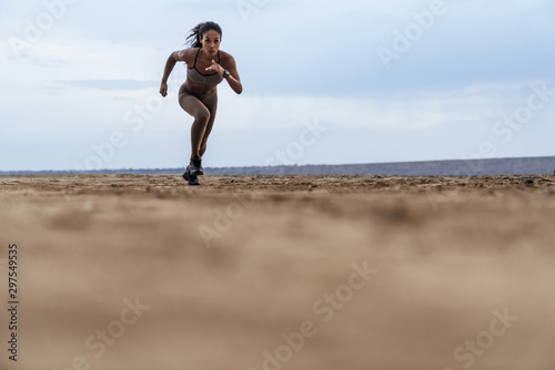Image of serious african american woman in sportswear running by seaside