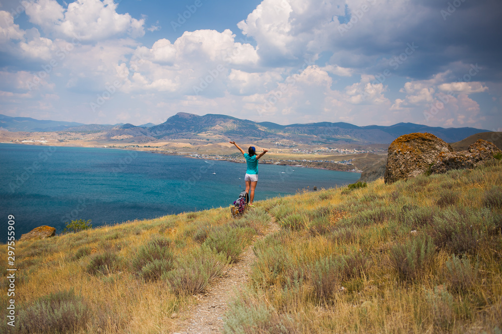 Girl backs with a backpack on the background of the sea bay with arms outstretched