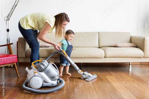 Mother and daughter using vacuum on hardwood floor at home