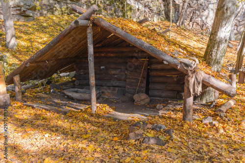 Dugout (or dug-out, pit-house, earth lodge, cellar dug) from logs in autumn forest. Traditional shelter for humans and livestock based on hole  into ground. Natural historical museum of dugouts photo
