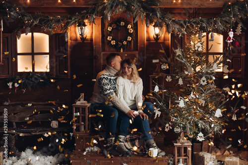 Christmas portrait of a romantic couple. They sit by a beautiful house and have hot coffee. New Year mood of lovers on the background of a wooden house, with fans. Close - up © Вячеслав Косько