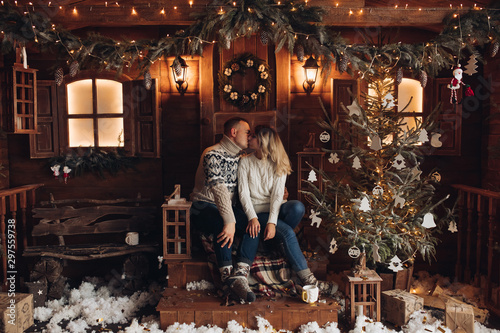 Christmas portrait of a romantic couple. Guy hugs the girl and kisses. They sit in a beautiful house. Christmas mood of lovers on the background of decorative snow and flying serpentine. Studio photo © Вячеслав Косько