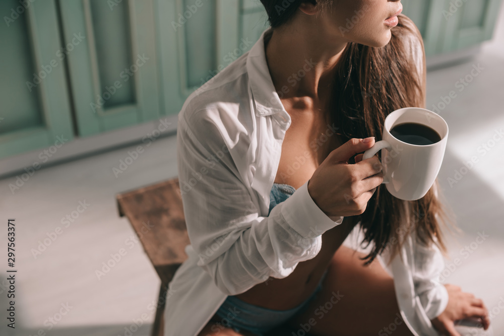 cropped view of woman in blue lingerie and white shirt holding cup of coffee in kitchen cropped view of woman in blue lingerie and white shirt holding cup of coffee in kitchen