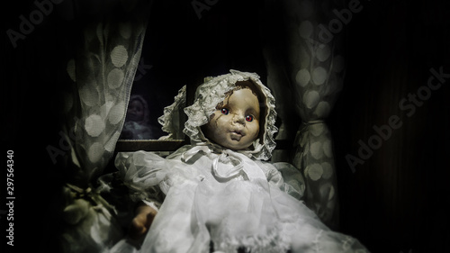 Foto horror vintage baby girl doll with scar face sit against the window, black vigne