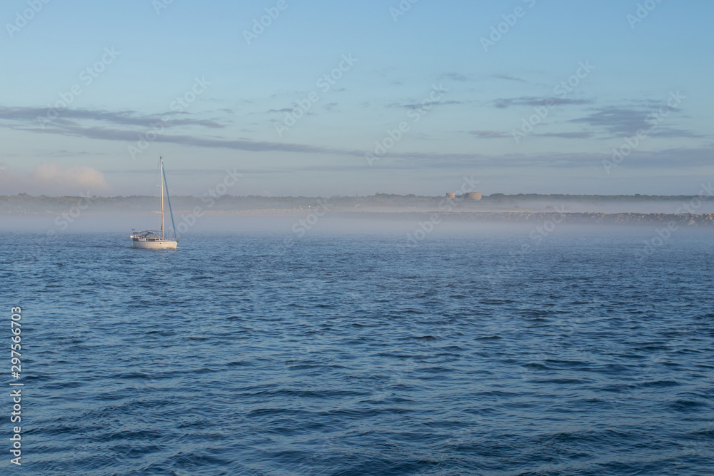 Fototapeta premium Big Catamaran Sail Boat Moored In A Calm Blue Harbour At Sunrise With Low Clouds In The Sky