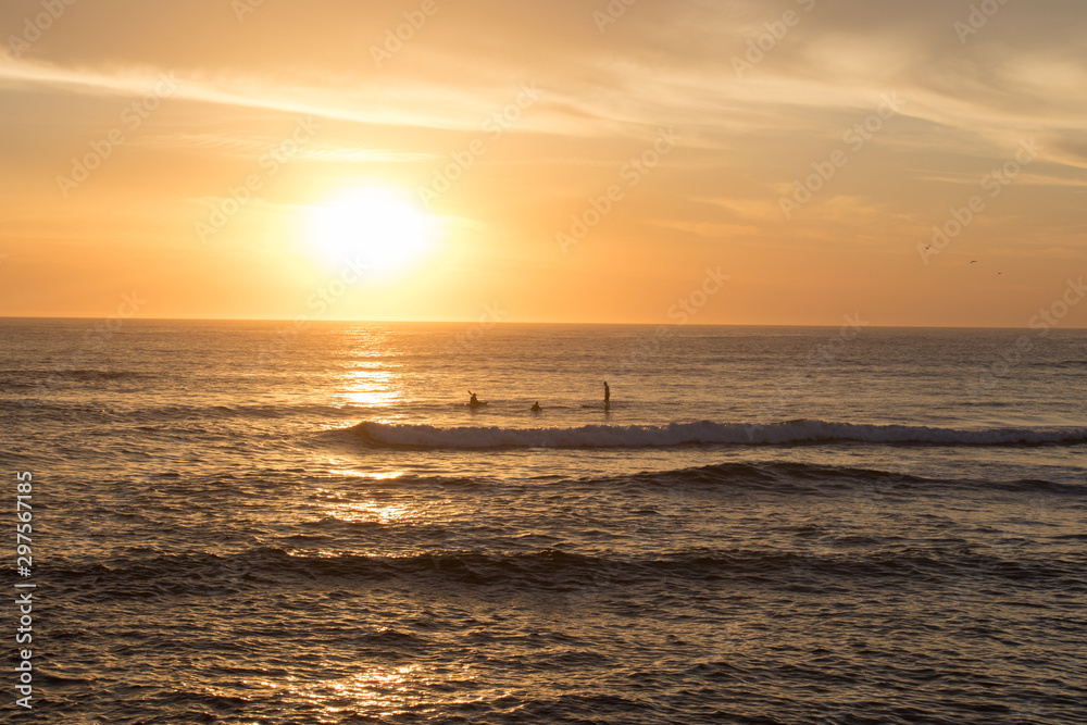 Golden Orange Sunrise With Waves Crashing And People On Kayaks And Paddle Boards In The Distance With Salt Spray In The Air