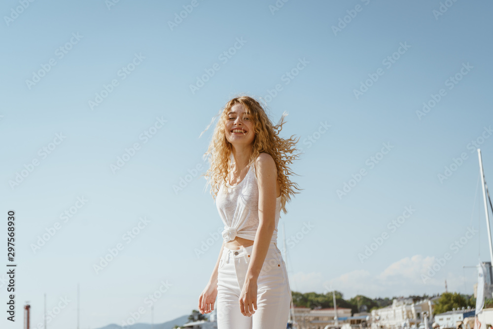 A joyful blonde with flying hair stands against the backdrop of a seaside landscape A joyful blonde with flying hair stands against the backdrop of a seaside landscape