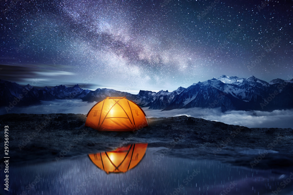 Camping adventure in the mountains. A tent pitched up and glowing under the milky way. Photo composite. - obrazy, fototapety, plakaty 
