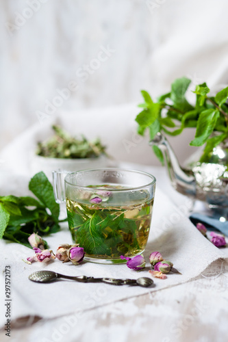 Traditional hot mint moroccan tea served in a transparent cup. Metal teapot with fresh mint on the background. Dry leaves and vintage spoon as decor. Gentle herbal detox, natural depressant