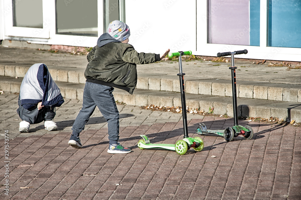 Boys on scooters. Fun sport. Children play with scooters. Children's sport.  Fun kids weekend. Brothers athletes. Photos | Adobe Stock