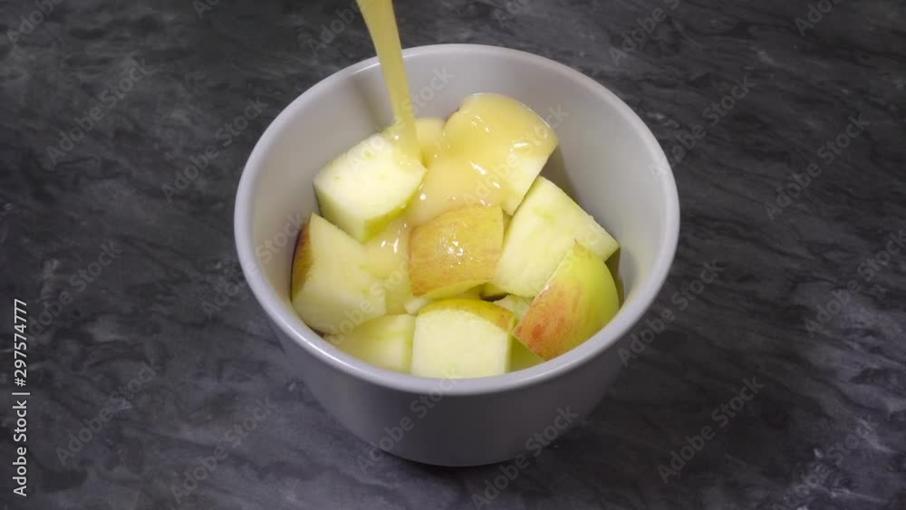 Close POV slow motion shot of hot, thick custard being poured over chopped apple pieces in a bowl on a granite surface.