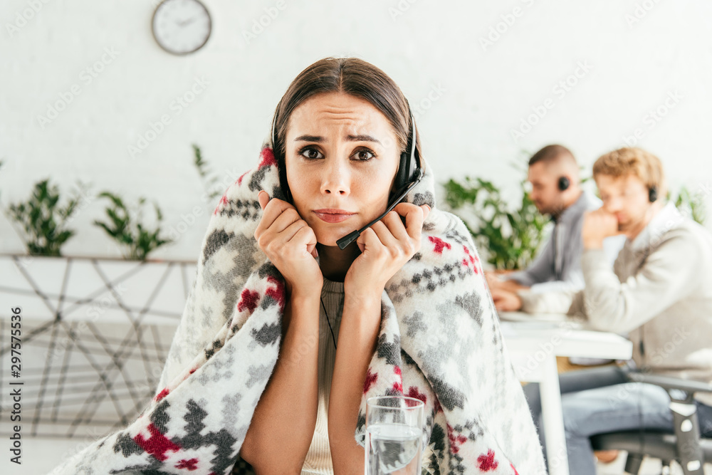 selective focus of sick broker wrapped in blanket looking at camera near coworkers selective focus of sick broker wrapped in blanket looking at camera near coworkers