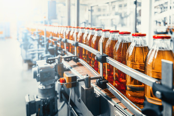 Conveyor belt, juice in glass bottles on beverage plant or factory interior, industrial manufacturing production line