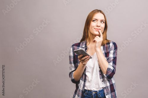 Photo of cheerful cute beautiful young woman chatting by mobile phone isolated over grey wall background.