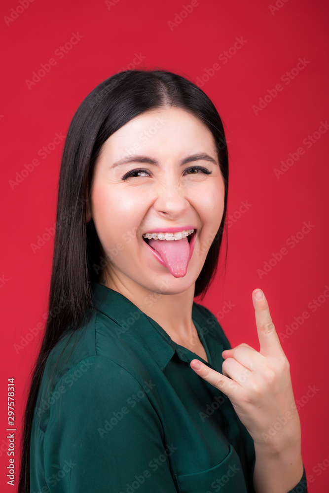 Portrait of a beautiful woman makes a grimace, opens her mouth wide and shows her tongue, on a red background Portrait of a beautiful woman makes a grimace, opens her mouth wide and shows her tongue, on a red background