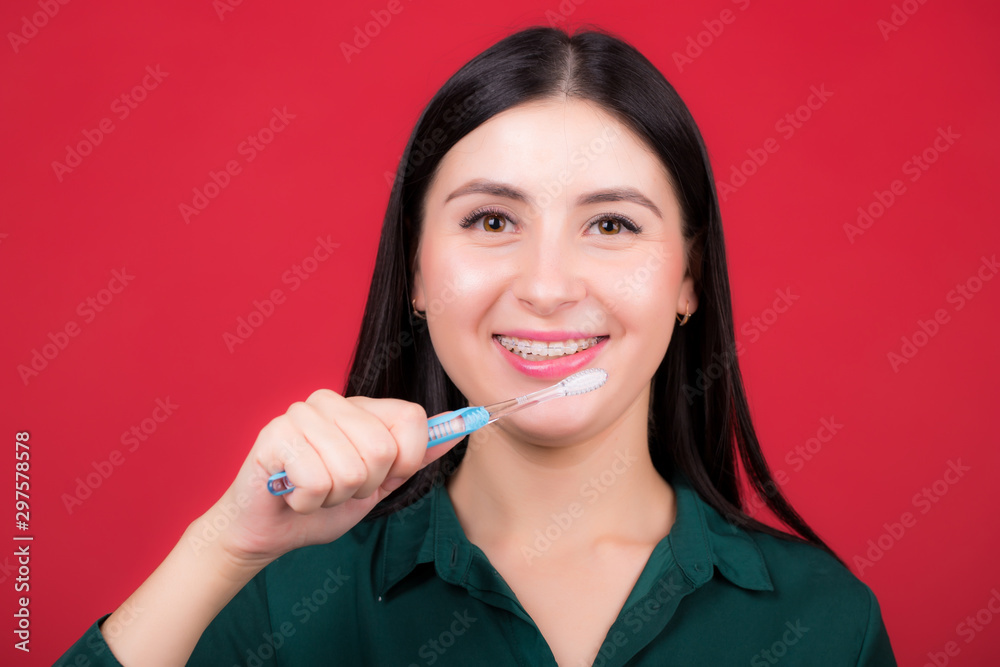 Young smiling woman with a toothbrush in hand, posing in studio on a red background Young smiling woman with a toothbrush in hand, posing in studio on a red background