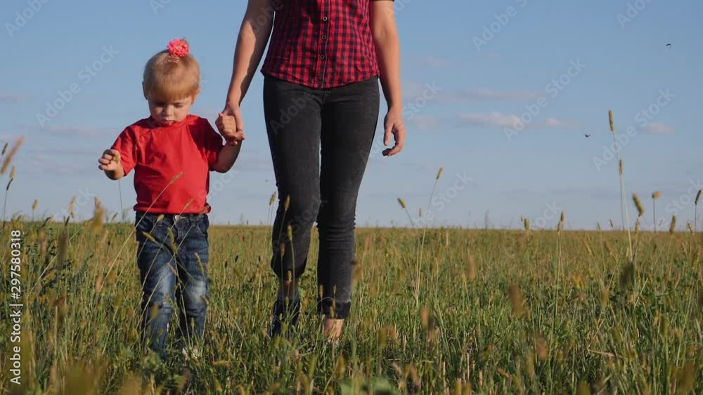 A young mother walks with her blonde daughter in the fresh air. Happy family walking on green grass. A young mother walks with her blonde daughter in the fresh air. Happy family walking on green grass.