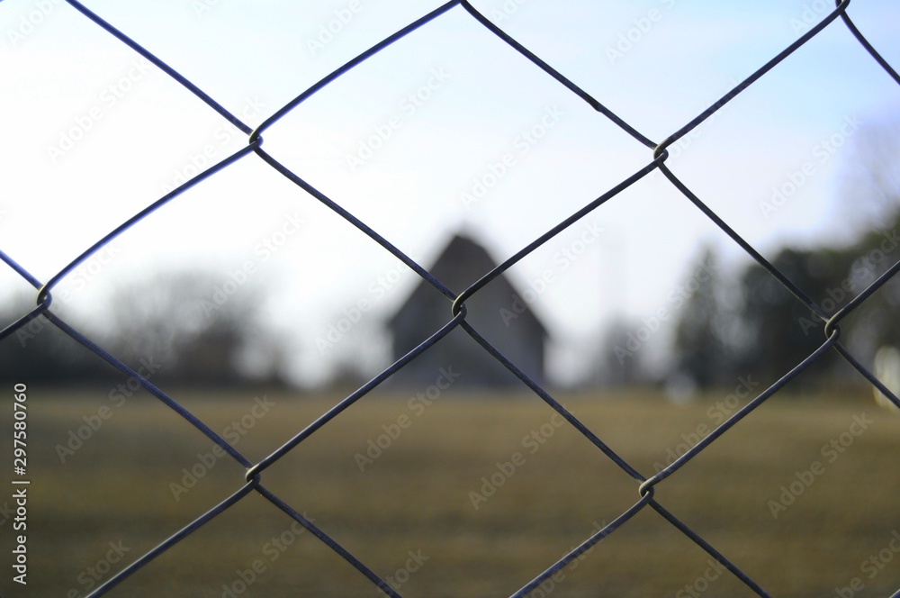 fence in the focus with a house and the field behind fence in the focus with a house and the field behind